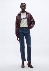 Burgundia nahast lühike jakk, valge kampsun tekstiga „Calvin Klein“, sinised kulunud teksad ja pruunid kontsaga pahkluu-saapad.