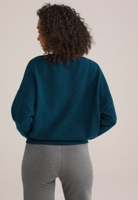 Tyrkysový oversized svetr s texturovanou tkaninou, uvolněný střih a žebrované manžety. V kombinaci se šedými přiléhavými legínami pro pohodlný look.