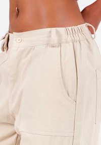 Beige broek met een elastische tailleband, voorzien van zijzakken en een relaxte pasvorm. De stof heeft een gladde, gestructureerde afwerking.