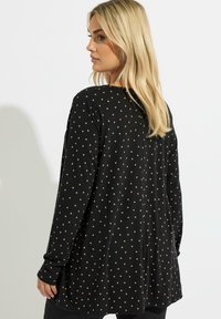 Haut noir à manches longues avec un design à côtes texturées et de petits pois beiges. Présente une coupe décontractée et un col rond.