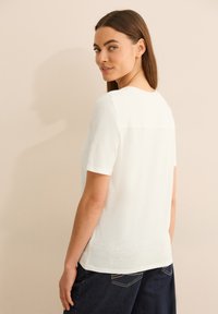 Witte T-shirt met korte mouwen van een licht gestructureerde stof, ronde halslijn en een rechte snit, gecombineerd met donkerblauwe jeans.