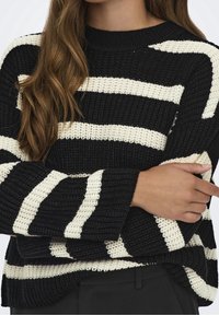 Black and ivory striped knitted sweater with a loose fit, long sleeves, and ribbed cuffs, featuring a textured pattern and crew neckline.
