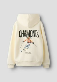 Kreemikas tumesinine kapuutsiga pusa, millel on tagaküljel suur kiri "CHAMONIX" ja graafika suusatajast, kes kannab oranži jakki ja siniseid pükse ning sõidab nõlval alla.