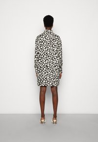 Zwarte bloemen jurk met witte bloemenpatronen, lange mouwen, een kraag en een losse fit, gecombineerd met lichte hakken.