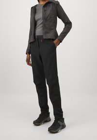 Musta kevyt takki hupulla, harmaa tiukkasti istuva paita ja mustat slim-fit-housut. Kengät ovat tummat, joissa on tekstuuriset yksityiskohdat ja pitävät pohjat.