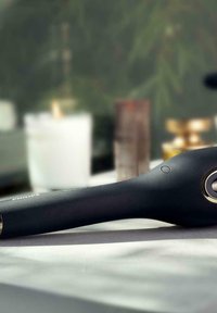 Schwarz, tragbares Gerät mit einem glatten Griff, silbernem Knopf und kreisförmigem goldenen Akzent nahe der Basis. Minimalistisches Design auf einer flachen Oberfläche.