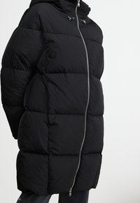 Black puffer coat with a hood, featuring a front zipper and a quilted design. The fabric appears smooth and insulated, providing warmth.