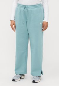 Lyseblå joggebukser med elastisk midje, snor, side lommer og løs passform. Kombinert med grå joggesko med svart aksent.