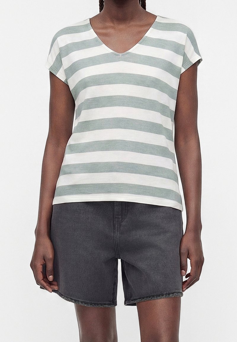 Personne portant un t-shirt à rayures blanches et gris clair avec col en V et manches courtes, associé à un short en denim gris foncé.