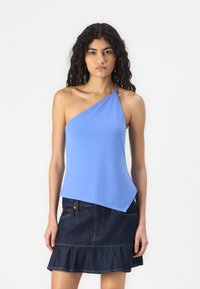 Top azul asimétrico hecho de una tela suave, con una tira en un hombro. Combinado con una falda de mezclilla oscura con un dobladillo con volantes.