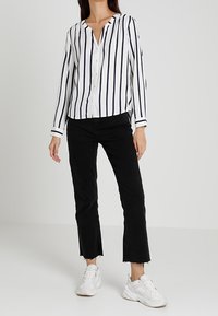 Hvid skjorte med marineblå lodrette striber, lange ærmer og V-hals. Sammen med sorte jeans med franje i kanten og hvide sneakers.