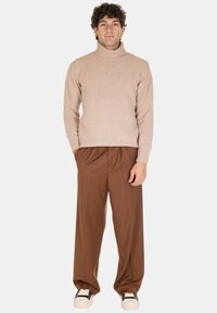 Maglione beige a collo alto abbinato a pantaloni marroni a gamba larga. L'outfit presenta una texture a costine nel maglione e una cintura elastica nei pantaloni.