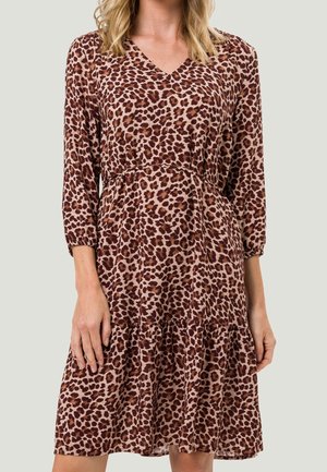 Femme portant une robe mi-longue, manches longues, col en V, avec un motif léopard marron et noir sur tissu marron clair.