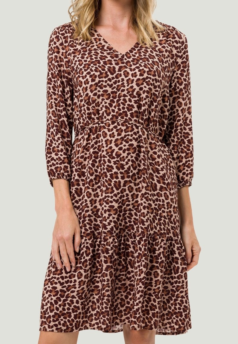 Femme portant une robe mi-longue, manches longues, col en V, avec un motif léopard marron et noir sur tissu marron clair.
