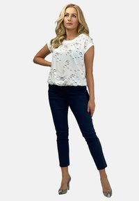 Biała bluzka z krótkim rękawem w czarny wzór ptaków, zestawiona z dopasowanymi granatowymi spodniami i teksturowanymi szarymi szpilkami. Prosty, nowoczesny design.