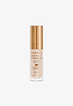 Kokie Doubletime Full Cover Concealer skaidriame stikliniame buteliuke su blizgiu auksiniu dangteliu; turi produkto pavadinimą ir detales atspausdintas auksinės spalvos šriftu.