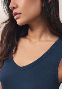 Ribbed navy tank top with a scoop neckline. Soft texture and fitted design, highlighting collarbone and shoulder details.
