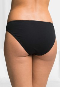 Bas de bikini noir en tissu lisse, avec une coupe taille basse et une couverture minimale. Coutures visibles le long des bords.