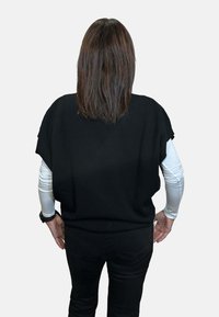 Top nero lavorato a maglia con maniche corte, caratterizzato da una vestibilità ampia e orlo a coste. Indossato sopra una camicia bianca a maniche lunghe, abbinato a pantaloni neri.