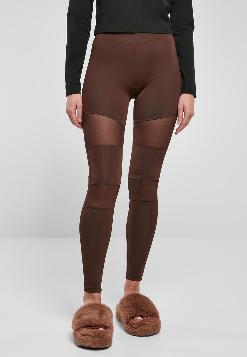 Leggings bruns à texture lisse, avec des panneaux transparents aux genoux et une taille haute, assortis à des chaussons bruns duveteux.
