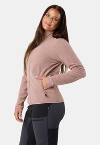 Jasnoróżowa polarowa kurtka z wysokim kołnierzem, zapinana na zamek z przodu oraz z bocznymi kieszeniami; charakteryzuje się gładką teksturą i dopasowanym krojem.