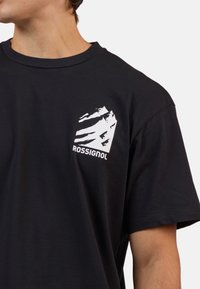Černé bavlněné tričko s bílým grafickým motivem hory a textem "ROSSIGNOL" na levé části hrudi. Klasický kulatý výstřih a krátké rukávy.