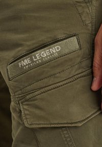 Olivengrüne Cargo-Hose aus strukturiertem Stoff, mit gesteppten Akzenten und einer Seitentasche, die das Logo "PME Legend American Classic" zeigt.