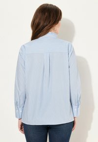 Camicia a righe blu chiaro con maniche lunghe, polsini a bottoni e colletto strutturato. Il retro presenta un giogo e dettagli di piega.