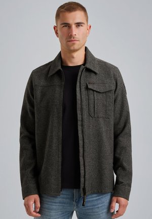 Grau melierte Wollmischjacke mit einem Reißverschluss, zwei Brusttaschen und einem Kragen, getragen über einem schwarzen Hemd und blauen Jeans.