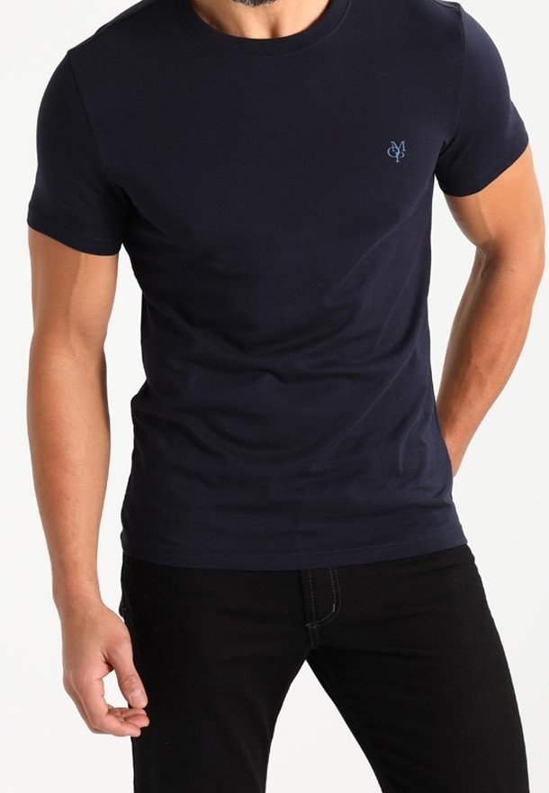 Homme portant un t-shirt bleu marine ajusté à manches courtes avec un petit logo bleu sur la poitrine gauche, assorti à un pantalon noir.