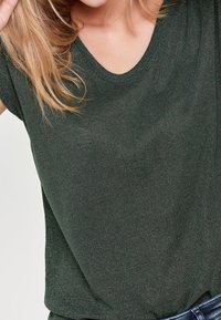 Mörkgrön, kortärmad topp med V-ringning. Tyget har en subtil lyster som ger struktur och djup åt materialet.