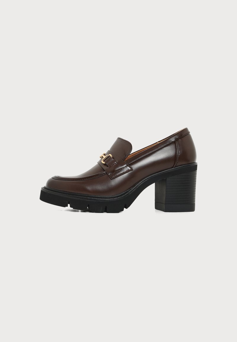 Mocassin marron en cuir à talon haut avec semelle noire épaisse et boucle décorative dorée sur fond blanc uni.