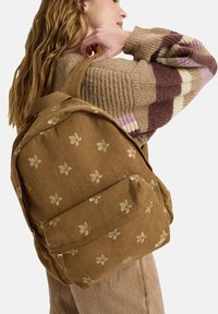 Brown corduroy backpack featuring gold floral embroidery, a zippered front pocket, and padded shoulder straps for comfort.