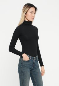 Svart langermet genser med høy hals i en tettsittende design, kombinert med medium vaskede denim jeans. Stoffet ser glatt og elastisk ut.