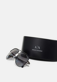 O pereche de ochelari de soare din metal negru, cu lentile gri în degrade, însoțiți de o carcasă elegantă neagră, care prezintă logo-ul și numele brandului „A/X”.