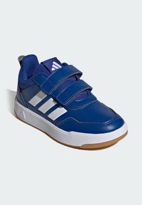 Niebieski skórzany but sportowy z dwoma zapięciami na rzep, białymi syntetycznymi paskami oraz brązową gumową podeszwą. Teksturowana tkanina na języku.