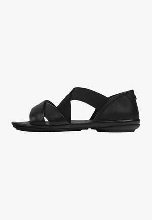 Black sandals featuring a combination of leather and elastic straps. Design includes crisscross upper, flat sole, and minimalistic silhouette.