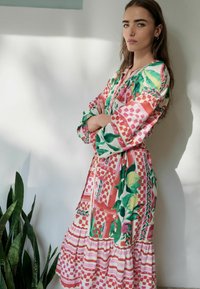 Rochie cu mâneci lungi, cu un model floral și geometric colorat, având un tiv volanțat și o croială lejeră, realizată dintr-un material ușor.