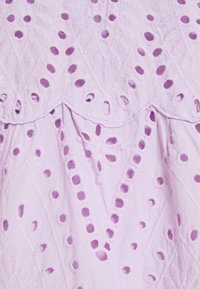 Fialová látka s propracovanou výšivkou a vyřezávanými vzory, včetně květinových motivů a vlnitých okrajů, vytvářející texturu a detaily.