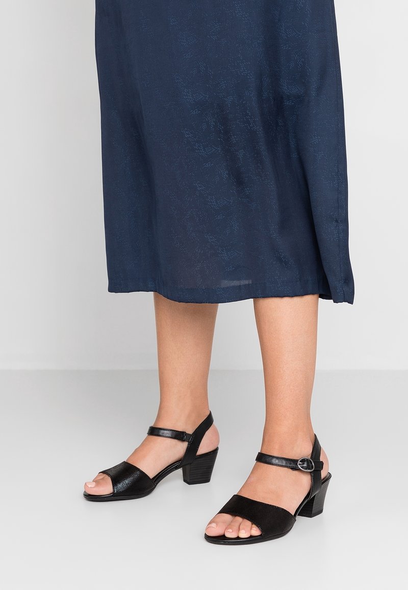 Svarta sandaler med en blandning av släta och texturerade material. Öppen tå-design, justerbar ankelrem och låg blockklack.