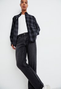 Zwart en grijs geruite blouse over een witte tanktop, gecombineerd met donkergrijze denim jeans en witte sneakers.