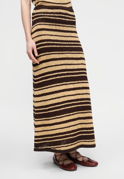 Πλεκτή μάξι φούστα με οριζόντιες καφέ και μπεζ ρίγες, με υφή υφάσματος. Συνδυάζεται με κόκκινα παπούτσια μπαλαρίνες με σταυρωτά λουράκια.