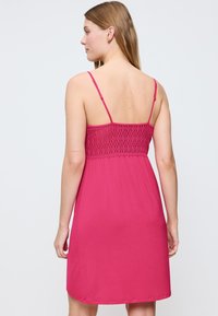 Abito rosa con spalline sottili e regolabili, dotato di un corpetto smock testurizzato e una gonna ampia. Finitura in tessuto morbido.