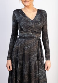 Musta kietaisumekko, jossa on pitkät hihat, V-pääntie ja paisley-kuvio metallinhohtoisissa hopea- ja kultaväreissä. Silkkinen, kevyt kangas.