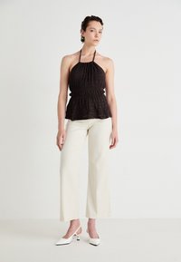 Haut à col halter noir avec des plis texturés, taille ajustée et ourlet en péplum, associé à un pantalon large blanc et des escarpins blanc à bride arrière.