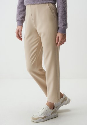 Beige op maat gemaakte broek met een gladde textuur, voorzien van voorplooien en een slim fit. Gepaarde met wit en beige sneakers.