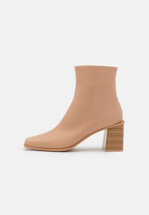 Bottine beige avec un bout pointu et un talon bloc en bois empilé de hauteur moyenne sur fond blanc.