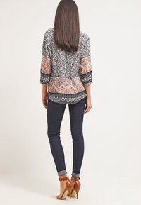 Blusa multicolor con patrones de paisley y flores, mangas tres cuartos y una combinación de colores en negro, blanco y coral, combinada con jeans oscuros.
