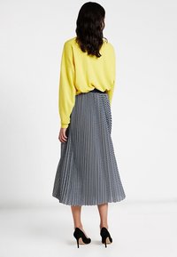 Felpa gialla a maniche lunghe abbinata a una gonna a righe bianche e nere lungo il ginocchio. Scarpe nere con tacco alto completano l'outfit.