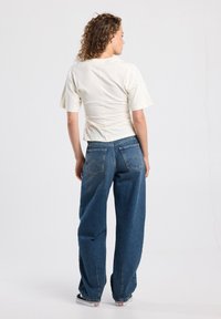 Cream short-sleeve top with back seam detailing paired with high-waisted blue wide-leg jeans featuring back pockets and subtle stitching accents.